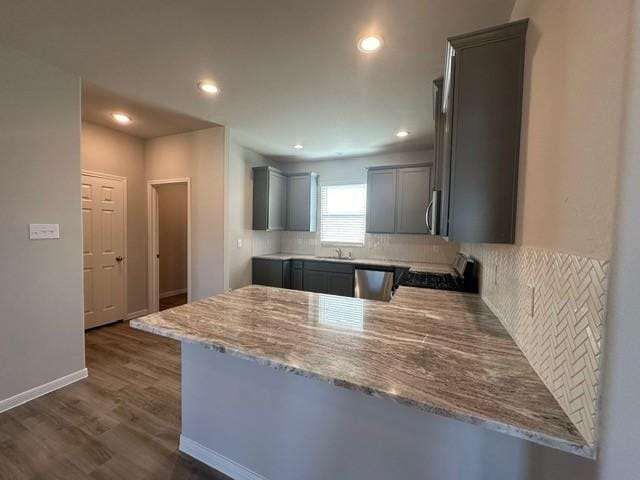 kitchen with kitchen peninsula, appliances with stainless steel finishes, light stone countertops, and dark wood-type flooring