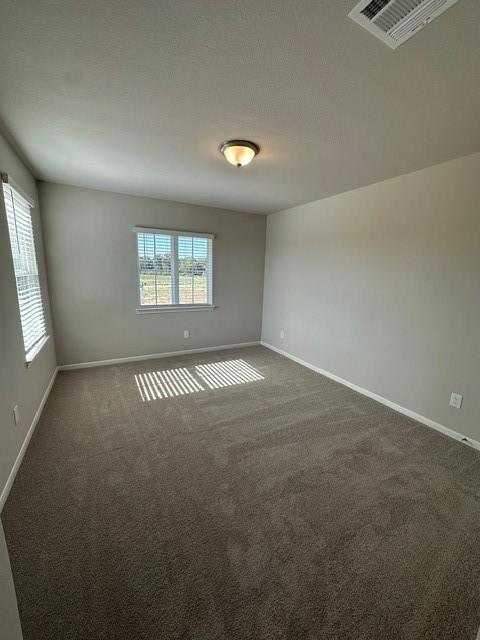 spare room featuring a wealth of natural light and dark colored carpet