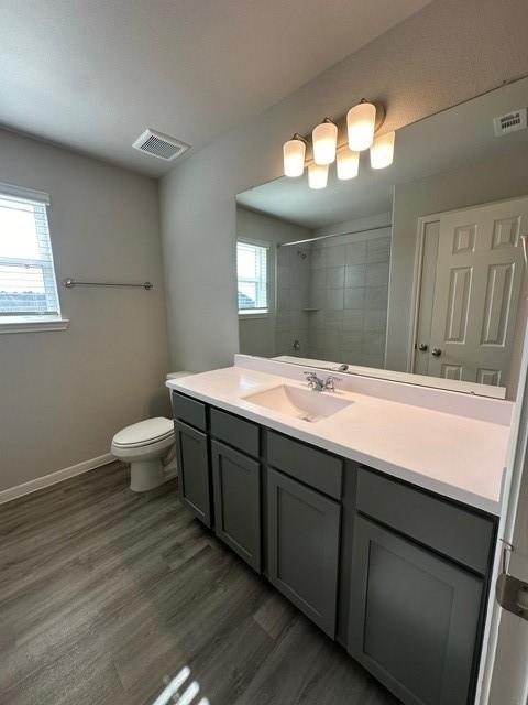 bathroom featuring tiled shower, vanity, hardwood / wood-style flooring, and toilet