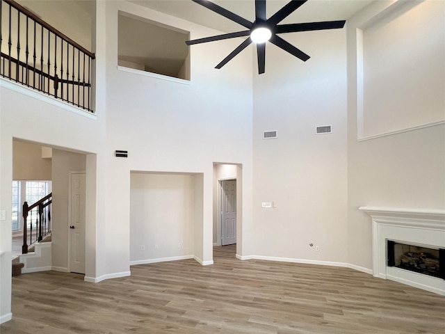 unfurnished living room featuring wood-type flooring, a towering ceiling, and ceiling fan