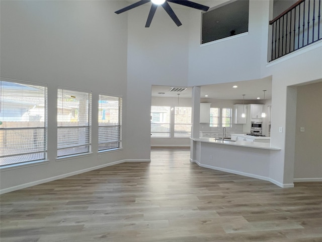 unfurnished living room with ceiling fan, light hardwood / wood-style flooring, a high ceiling, and sink