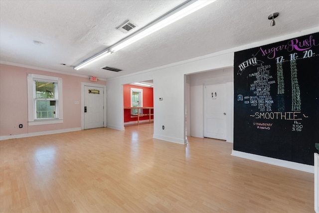 empty room featuring a textured ceiling, light wood-type flooring, and ornamental molding