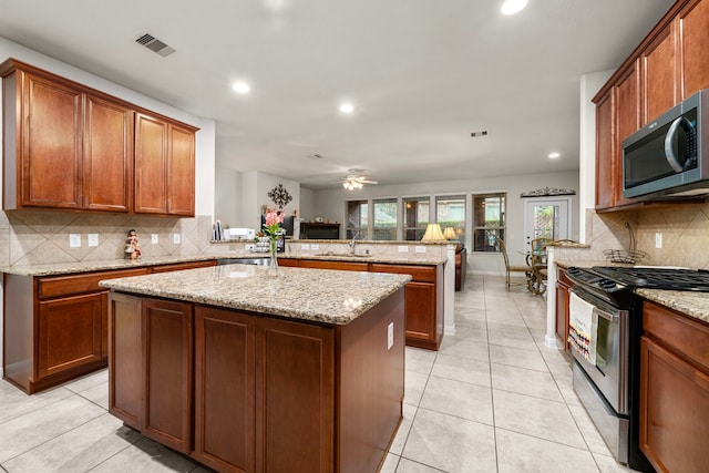 kitchen with light stone counters, stainless steel appliances, kitchen peninsula, and a kitchen island