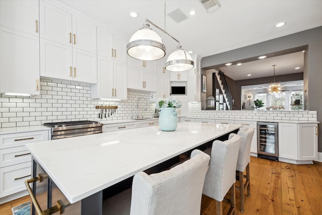 kitchen featuring white cabinets, decorative light fixtures, wine cooler, and a breakfast bar area