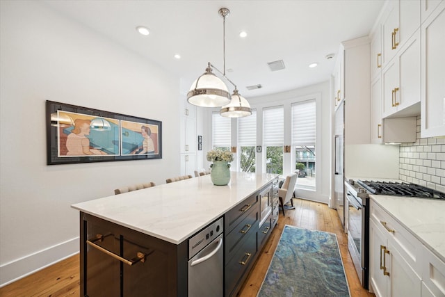 kitchen with decorative backsplash, stainless steel range, light hardwood / wood-style floors, white cabinetry, and hanging light fixtures