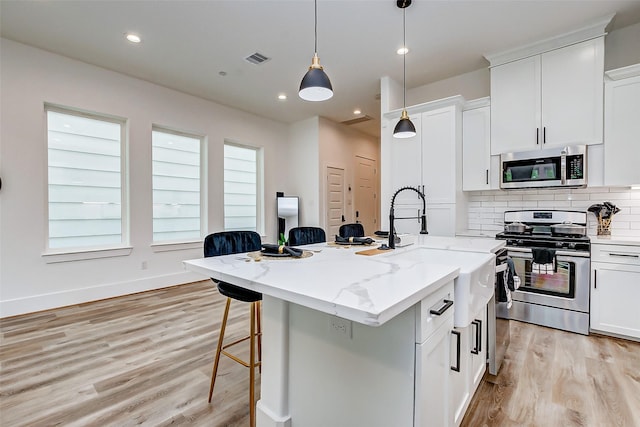 kitchen with a center island with sink, white cabinets, decorative light fixtures, light stone counters, and stainless steel appliances