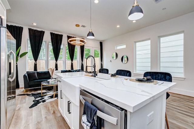 kitchen with stainless steel appliances, decorative light fixtures, a kitchen island with sink, a breakfast bar, and white cabinets