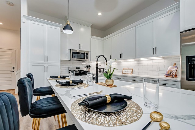 kitchen featuring light stone countertops, hanging light fixtures, white cabinets, and stainless steel appliances