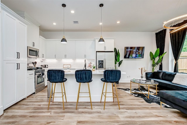 kitchen with white cabinetry, a center island with sink, decorative light fixtures, and appliances with stainless steel finishes