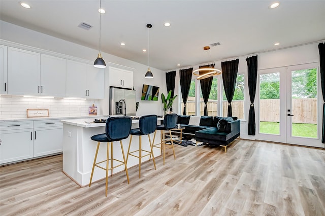 kitchen featuring white cabinetry, a center island with sink, decorative light fixtures, and light hardwood / wood-style flooring