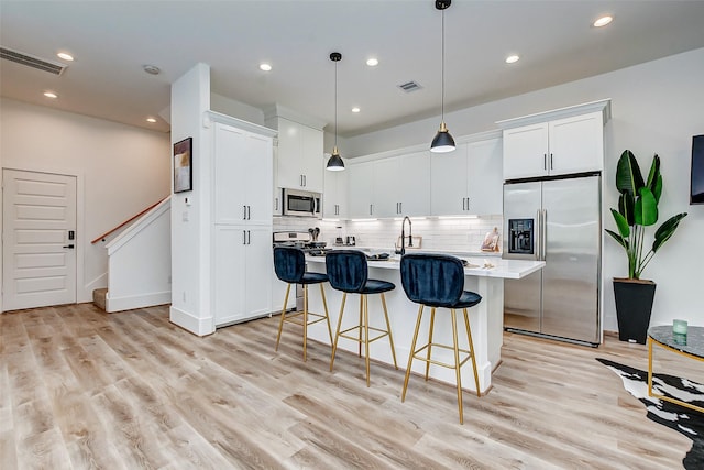 kitchen with a kitchen island with sink, pendant lighting, white cabinets, and stainless steel appliances