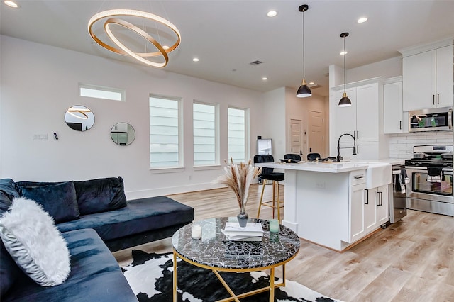 living room featuring an inviting chandelier, light hardwood / wood-style flooring, a healthy amount of sunlight, and sink