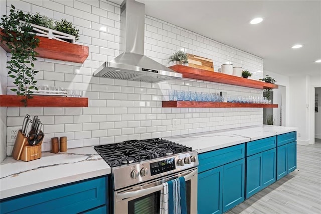 kitchen with wall chimney range hood, high end stainless steel range oven, blue cabinetry, tasteful backsplash, and light stone counters