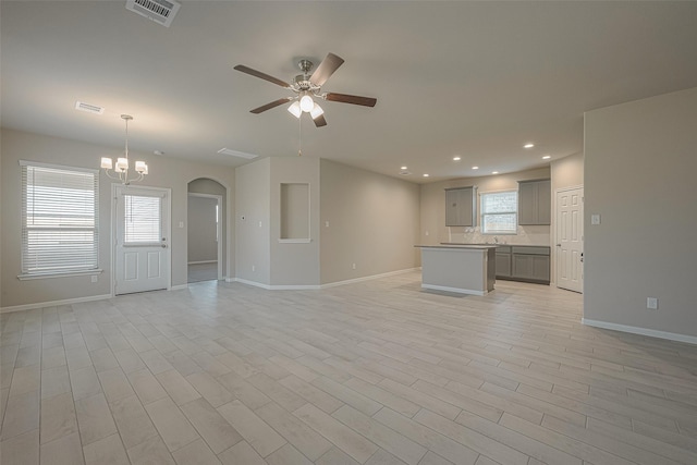 unfurnished living room with ceiling fan with notable chandelier, light hardwood / wood-style floors, and a wealth of natural light