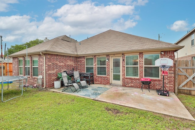 rear view of property featuring a yard, a patio, and a trampoline