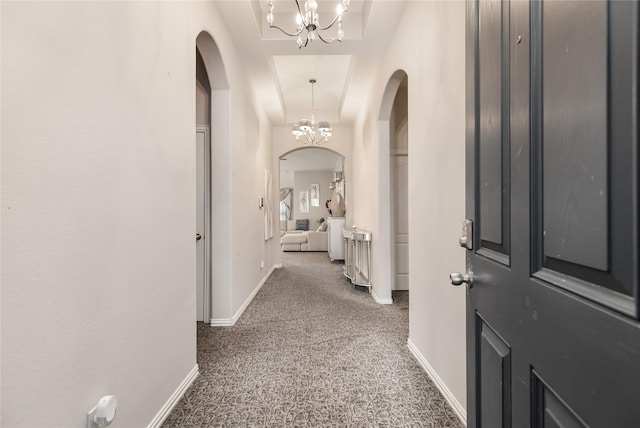 corridor with a raised ceiling and a notable chandelier