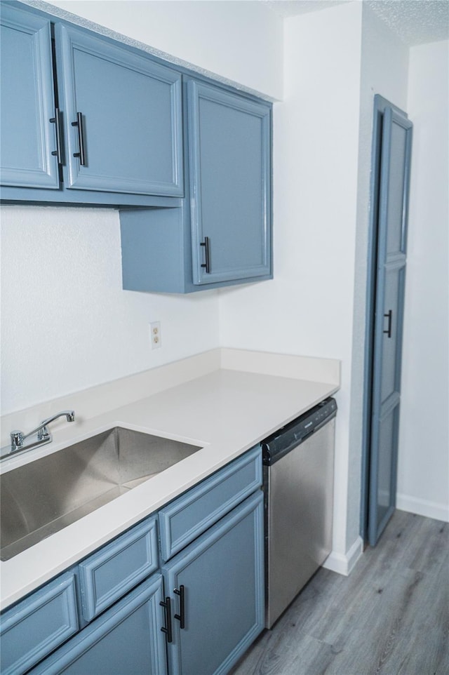 kitchen with blue cabinetry, sink, stainless steel dishwasher, and light wood-type flooring