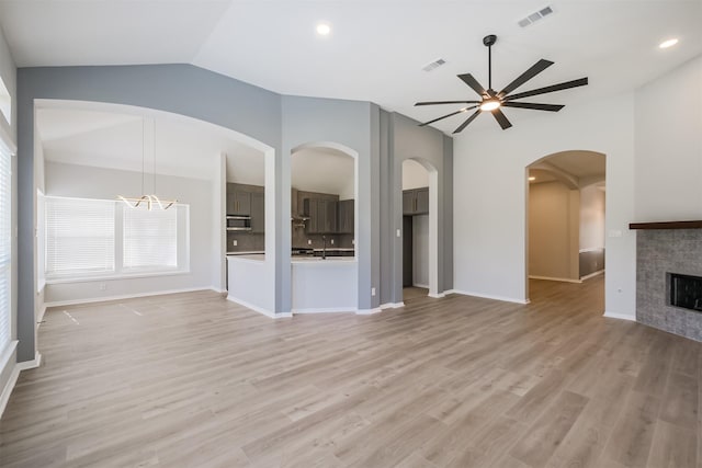 unfurnished living room with a tiled fireplace, lofted ceiling, ceiling fan with notable chandelier, and light wood-type flooring