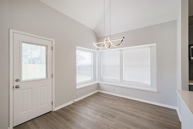 unfurnished dining area featuring light hardwood / wood-style flooring, a healthy amount of sunlight, vaulted ceiling, and a notable chandelier