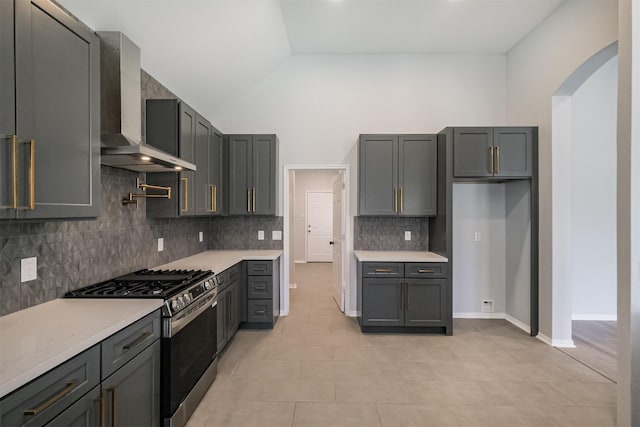 kitchen with wall chimney exhaust hood, gray cabinets, light stone countertops, light tile patterned floors, and stainless steel range with gas stovetop