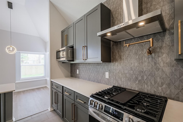 kitchen with hanging light fixtures, stainless steel appliances, wall chimney range hood, lofted ceiling, and light tile patterned floors