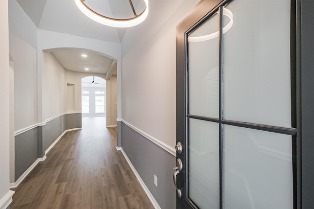 hall with baseboards, arched walkways, and wood finished floors