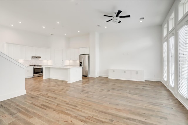 unfurnished living room featuring a towering ceiling, light hardwood / wood-style floors, ceiling fan, and sink