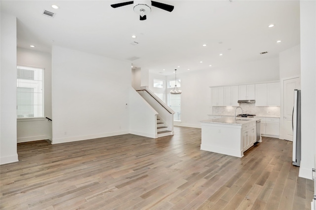 kitchen featuring ceiling fan with notable chandelier, stainless steel fridge, light wood-type flooring, an island with sink, and white cabinetry