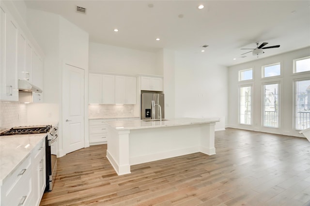 kitchen with ceiling fan, decorative backsplash, an island with sink, appliances with stainless steel finishes, and white cabinetry