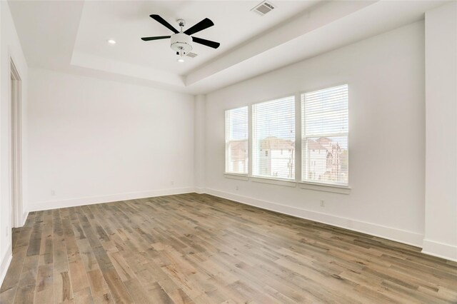 spare room with a tray ceiling, ceiling fan, and light hardwood / wood-style floors