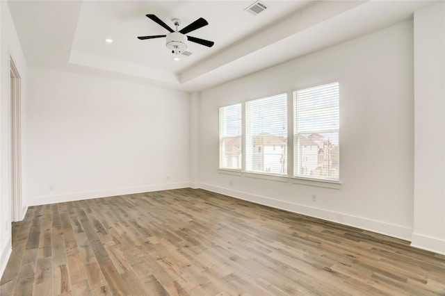 spare room featuring a tray ceiling, visible vents, baseboards, and wood finished floors