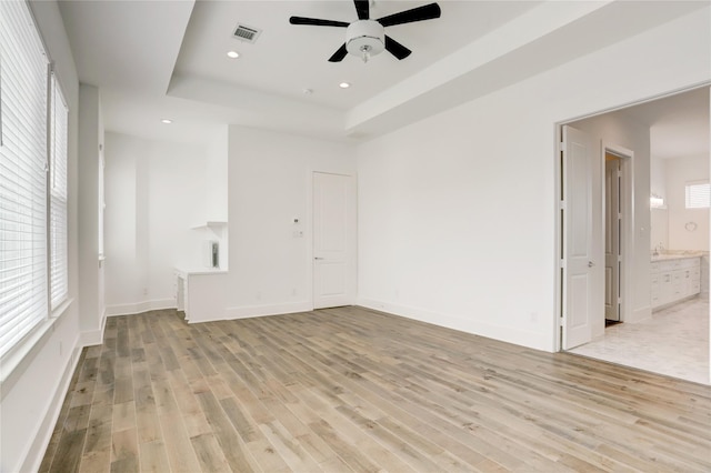 spare room with a raised ceiling, ceiling fan, and light wood-type flooring