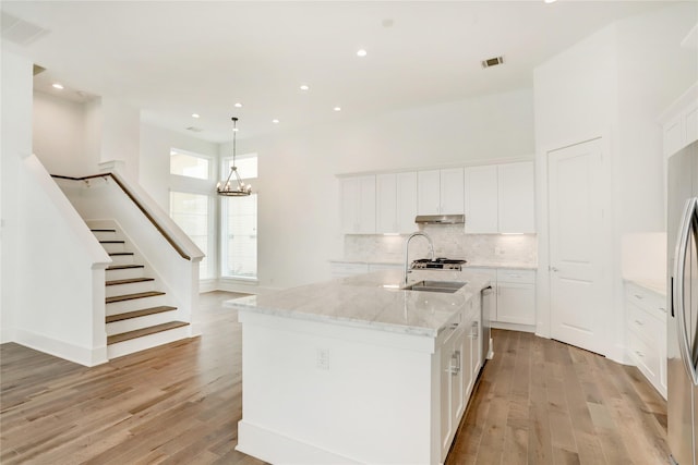 kitchen featuring light stone countertops, sink, white cabinetry, and an island with sink