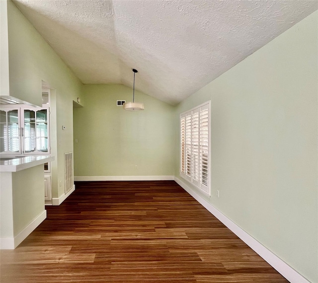 unfurnished dining area featuring a textured ceiling, dark hardwood / wood-style flooring, and vaulted ceiling