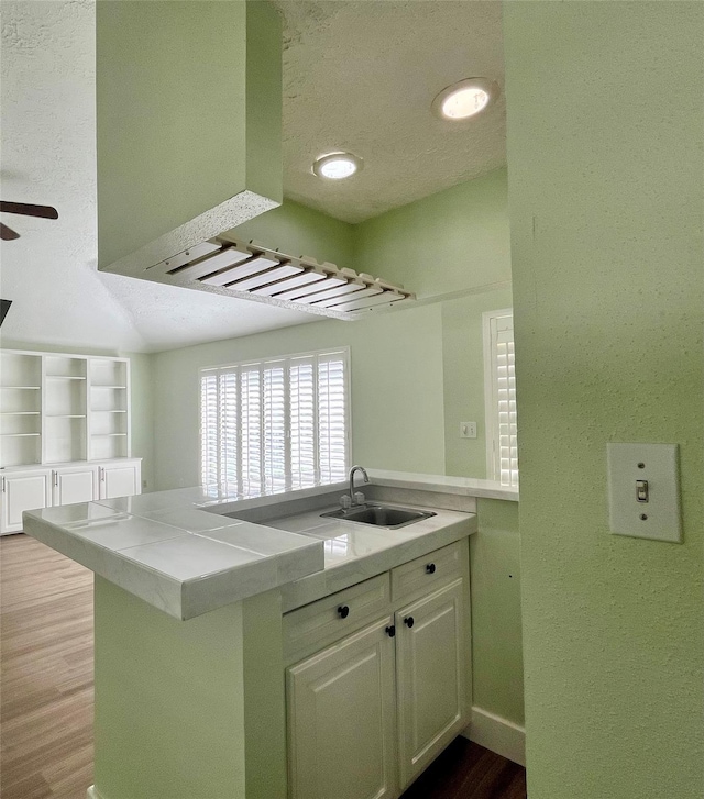 kitchen with sink, kitchen peninsula, light hardwood / wood-style floors, a textured ceiling, and white cabinets