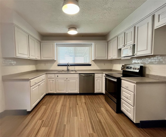 kitchen with white cabinets, appliances with stainless steel finishes, light hardwood / wood-style flooring, and sink