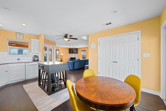 dining space with a tile fireplace, french doors, ceiling fan, and dark wood-type flooring