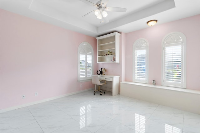 office space featuring a tray ceiling, ceiling fan, and built in desk