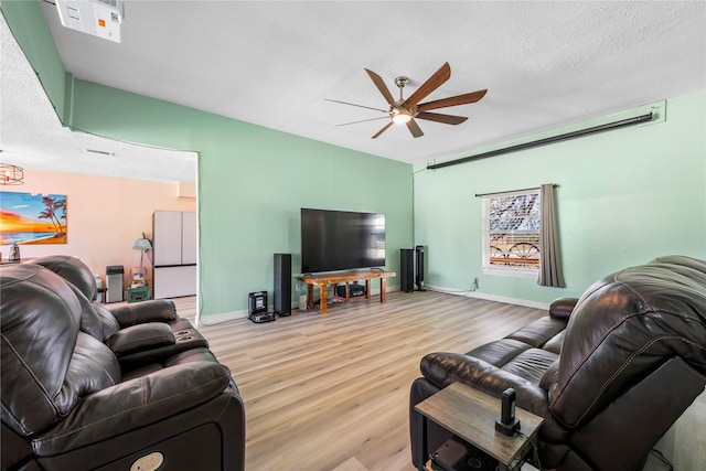 living room with ceiling fan, a textured ceiling, and light wood-type flooring