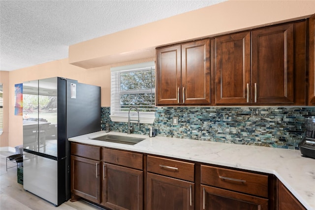 kitchen with stainless steel refrigerator, sink, tasteful backsplash, light stone counters, and a textured ceiling