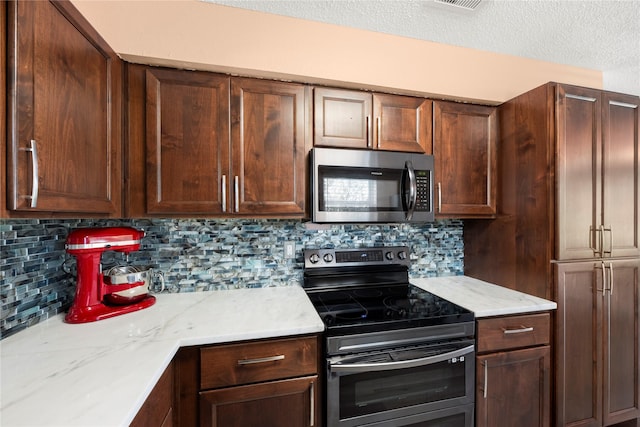 kitchen with a textured ceiling, light stone counters, stainless steel appliances, and tasteful backsplash