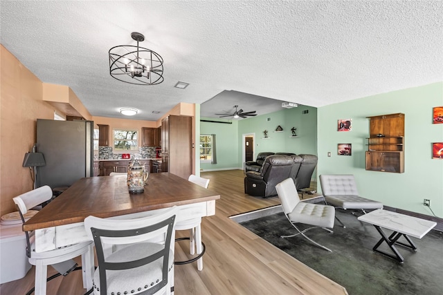 dining room featuring a textured ceiling, light hardwood / wood-style flooring, and ceiling fan with notable chandelier