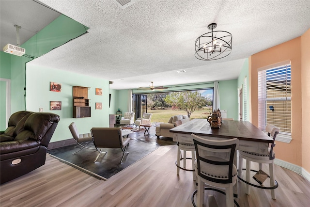 dining area with ceiling fan with notable chandelier, a wealth of natural light, and light hardwood / wood-style flooring