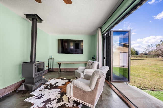 living room with ceiling fan, a healthy amount of sunlight, a wood stove, and a textured ceiling