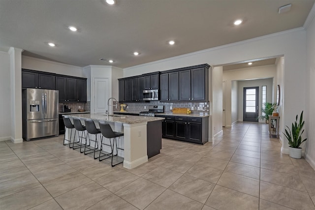 kitchen with light stone counters, stainless steel appliances, sink, an island with sink, and light tile patterned flooring