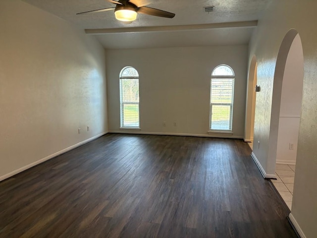 unfurnished room featuring beam ceiling, dark wood-type flooring, ceiling fan, and a healthy amount of sunlight