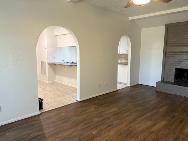 unfurnished living room with ceiling fan, wood-type flooring, a textured ceiling, and a brick fireplace