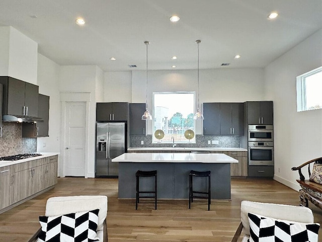 kitchen with a center island, a kitchen breakfast bar, decorative light fixtures, decorative backsplash, and appliances with stainless steel finishes