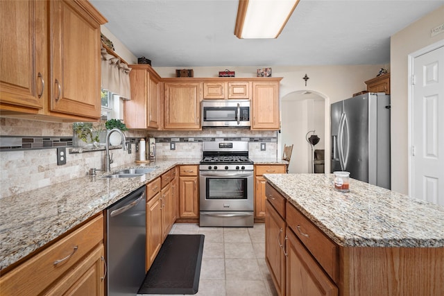 kitchen with a center island, sink, appliances with stainless steel finishes, tasteful backsplash, and light tile patterned flooring