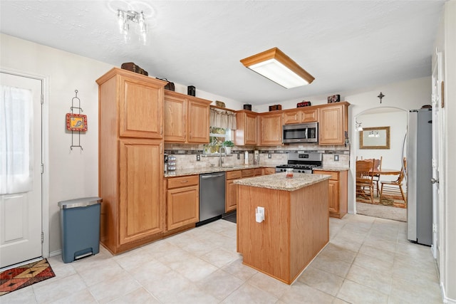 kitchen with light stone countertops, sink, decorative backsplash, a kitchen island, and appliances with stainless steel finishes